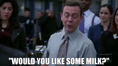 a man in a suit and tie is standing in front of a group of people and says would you like some milk ?