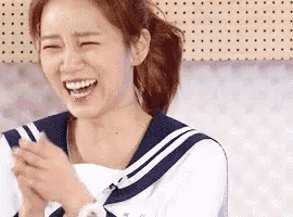 a woman in a sailor suit is laughing with her eyes closed and her hands folded .