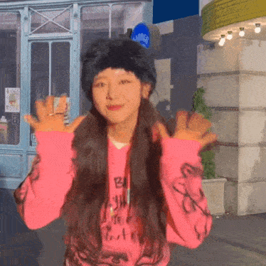 a girl wearing a pink sweatshirt and a black hat is standing in front of a building .