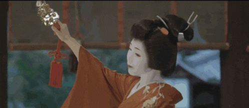 a woman in a red kimono is holding a sword with a red tag attached to it