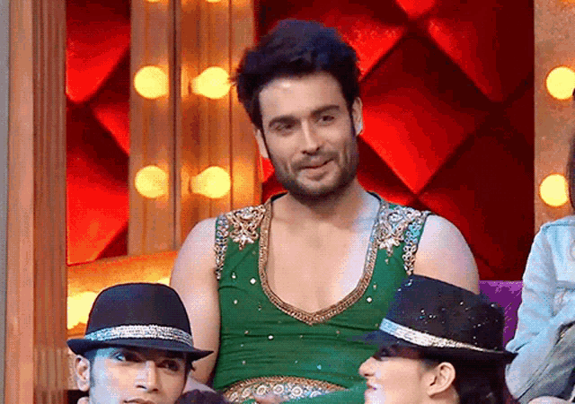 a man in a green dress is sitting next to two men wearing hats