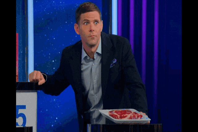a man in a suit holds a plate of meat in front of a sign with the number 5 on it