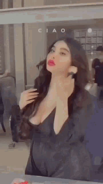 a woman in a black dress is standing in front of a mirror and adjusting her hair .