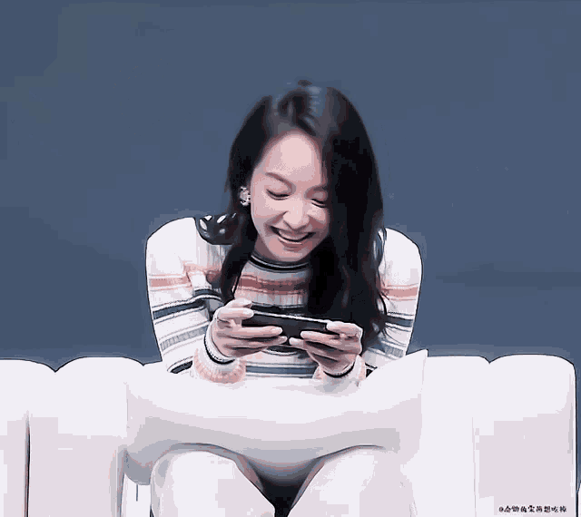 a woman is sitting on a couch playing a game on her phone with a blue background