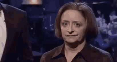 a woman in a black shirt is making a funny face while standing in front of a man in a suit .