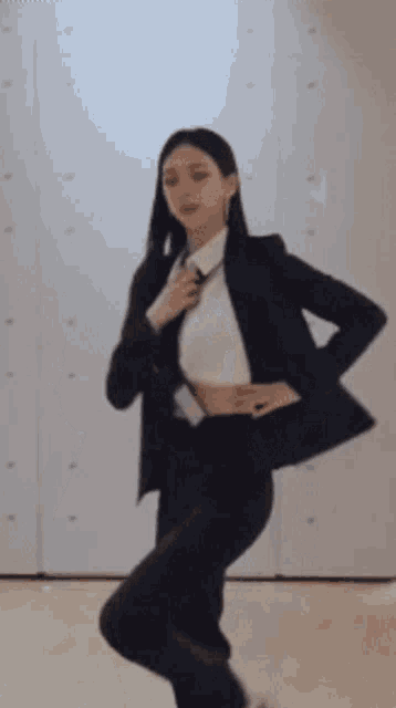 a woman is standing in a room wearing a suit and tie .