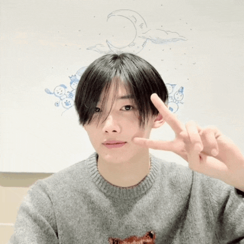 a young man making a peace sign in front of a white board