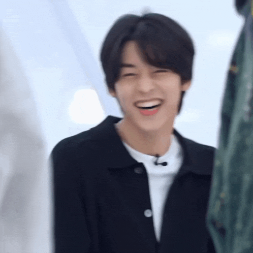 a young man in a black jacket is smiling and laughing .
