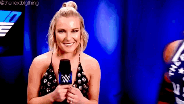 a woman is holding a microphone in front of a blue background and smiling .