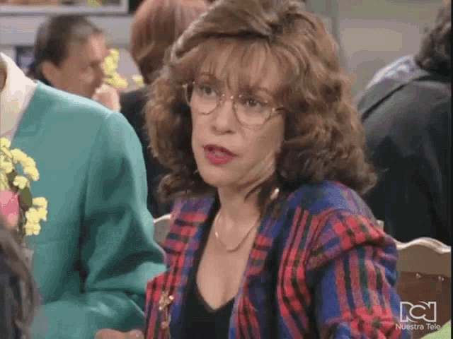 a woman wearing glasses is sitting at a table with other people