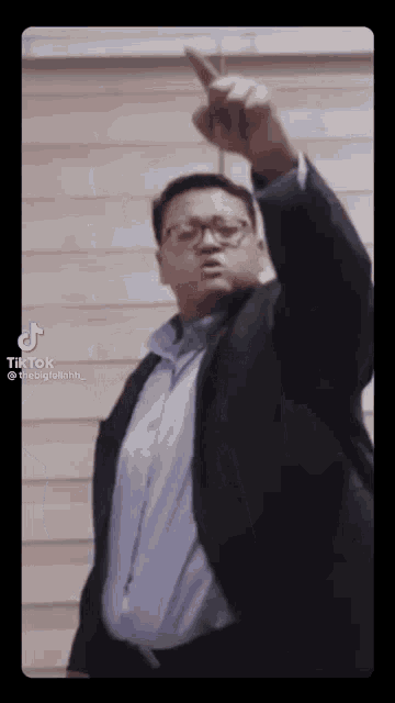 a man in a suit and glasses is pointing up with his finger