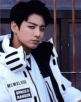 a young man wearing a white jacket with space ranger written on it is standing in front of a building .