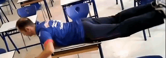 a man in a blue shirt is laying on a desk in a classroom .