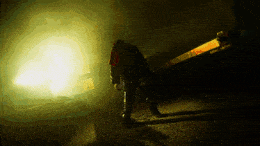a person holding a chainsaw in a dark room with a yellow light