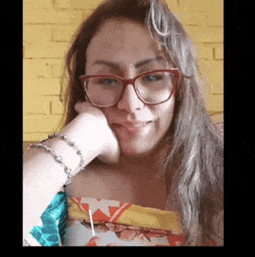 a woman wearing glasses and a bracelet holds her hand to her face