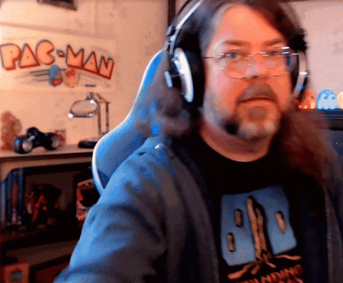 a man wearing headphones sits in front of a pac man poster