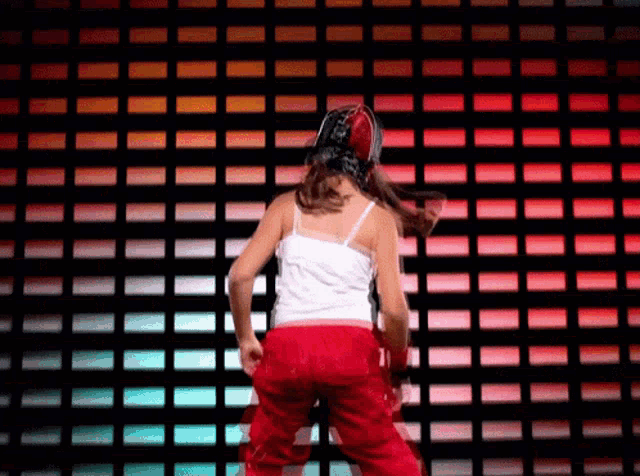 a woman in red pants is dancing in front of a wall with red lights .
