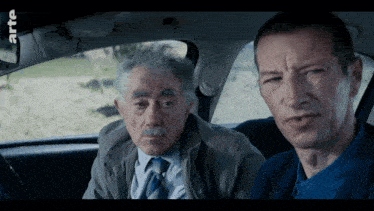two men sitting in a car with the word arte on the bottom right