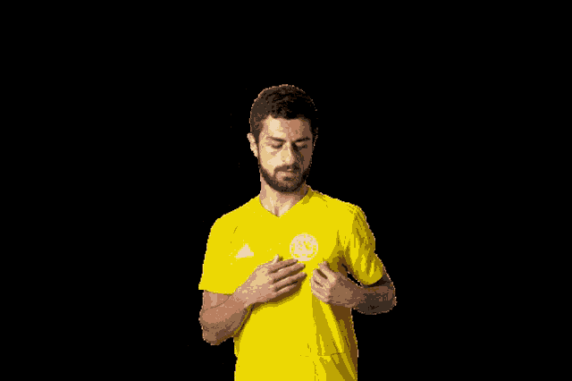 a man wearing a yellow adidas shirt holds his hands to his chest