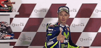 a motorcycle racer is giving a thumbs up in front of a checkered wall