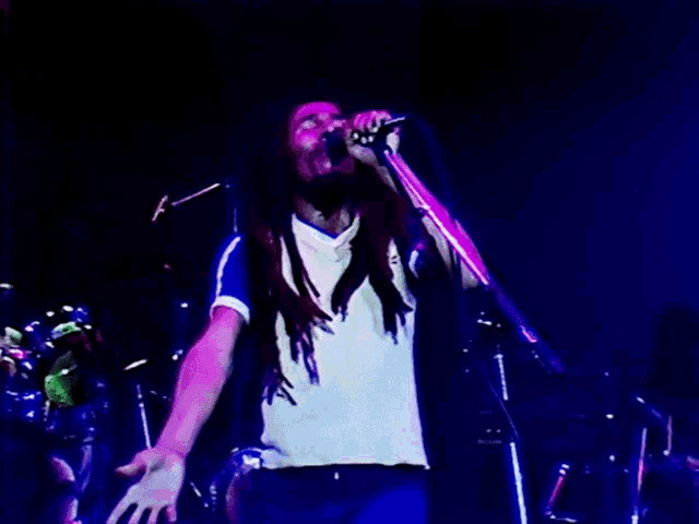 a man with dreadlocks singing into a microphone on a stage
