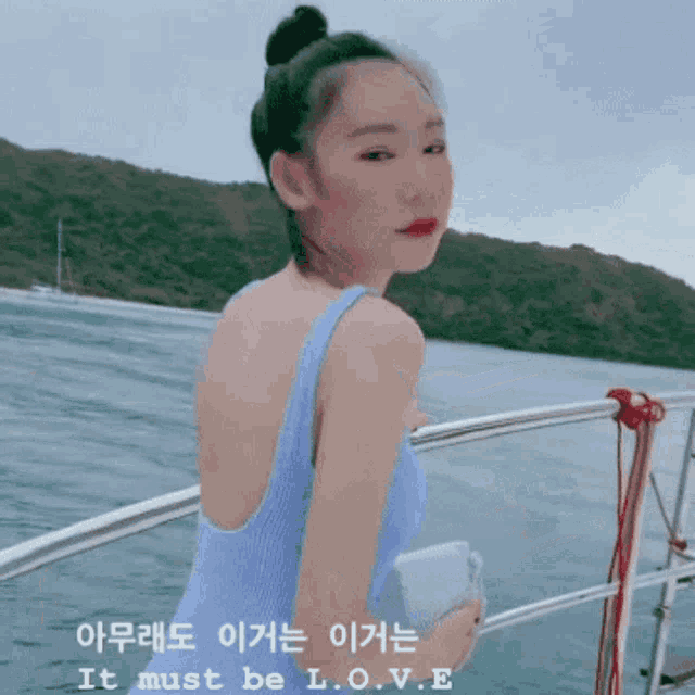 a woman in a blue swimsuit is standing on a boat with the words " it must be love " on the bottom