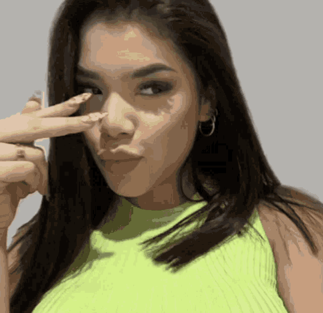 a woman in a neon green tank top is making a peace sign with her finger