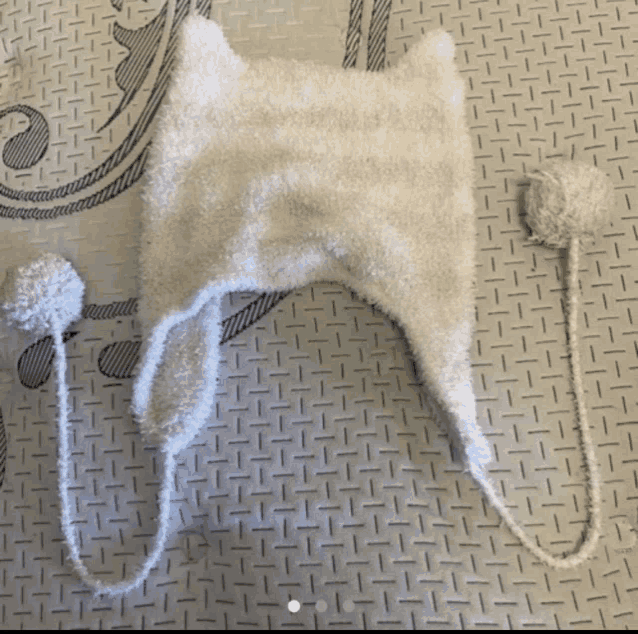 a white hat with two pom poms is laying on a grey surface