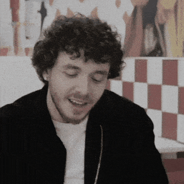a young man with curly hair and a beard is smiling