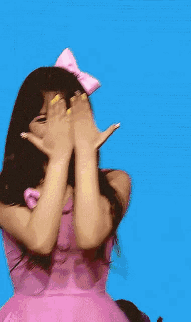 a woman in a pink dress with a pink bow on her head is covering her face with her hands