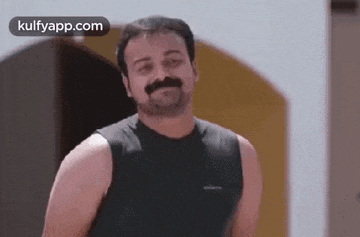 a man with a mustache wearing a black tank top is smiling .