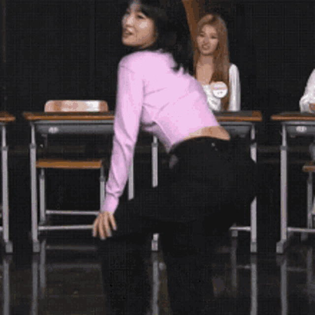 a woman in a purple sweater is standing in front of a group of people in a classroom .