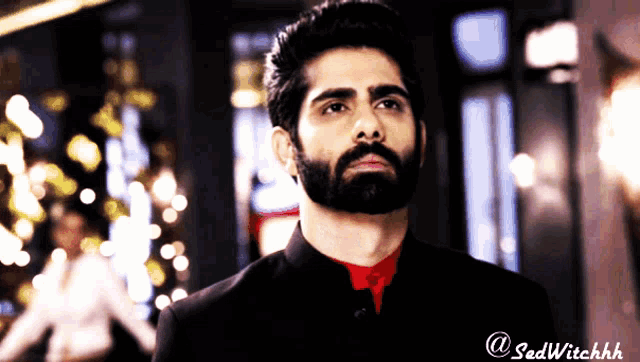 a man with a beard wearing a black suit and a red shirt