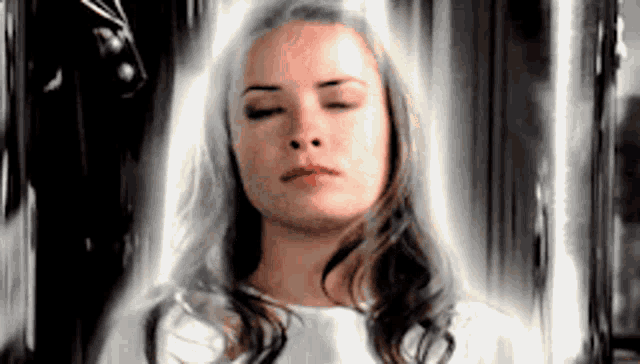a woman with her eyes closed is standing in front of a window with a white light coming out of it .