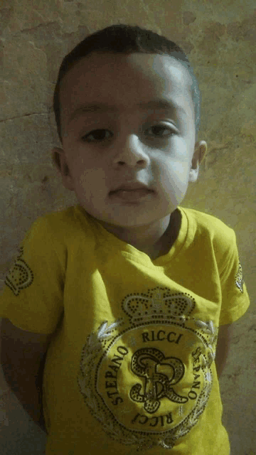 a little boy wearing a yellow shirt that says ricci on it