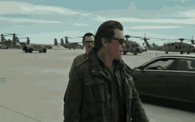 a man wearing sunglasses walks next to a man wearing glasses