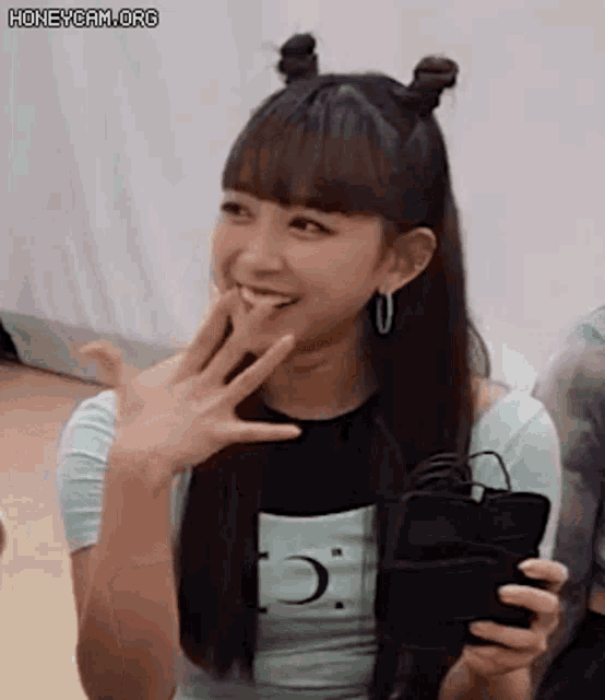 a young woman with two buns in her hair is smiling while holding a cell phone .