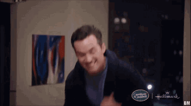 a man is standing in a room with a painting on the wall and laughing .
