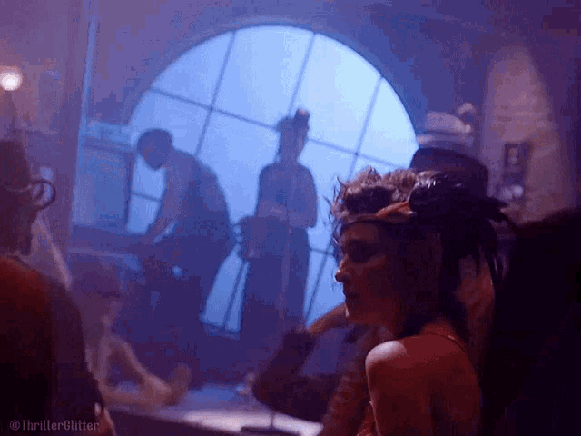 a woman in a red dress is standing in front of a window in a dark room with other people .
