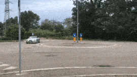 a car is driving around a roundabout with two blue signs on the side