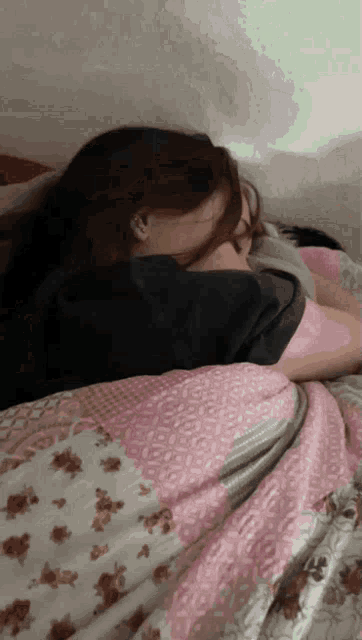 a woman is sleeping on a bed with a pink and white blanket