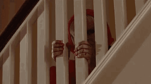 a person in a red hoodie is peeking through the railing of a staircase .