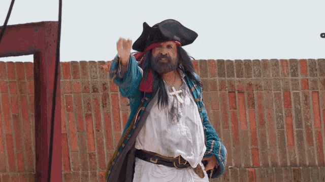 a man dressed as a pirate is standing in front of a red brick wall