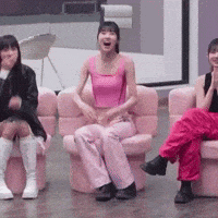 three girls are sitting in pink chairs and one is wearing a pink tank top