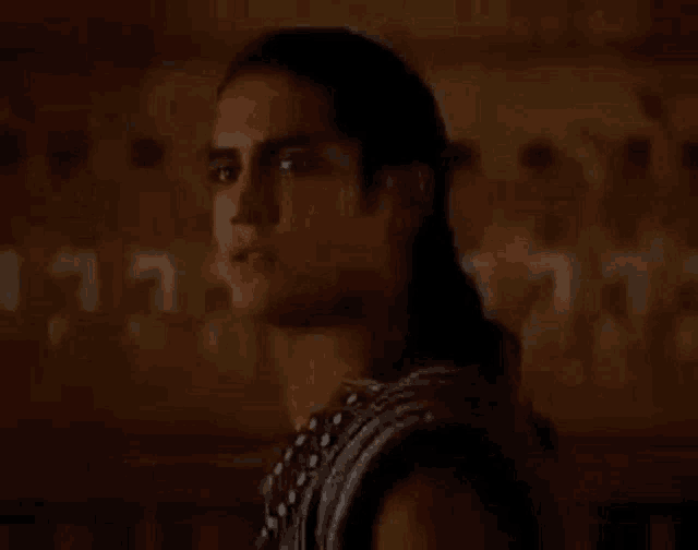 a man with long hair is standing in front of a wall and looking to the side .