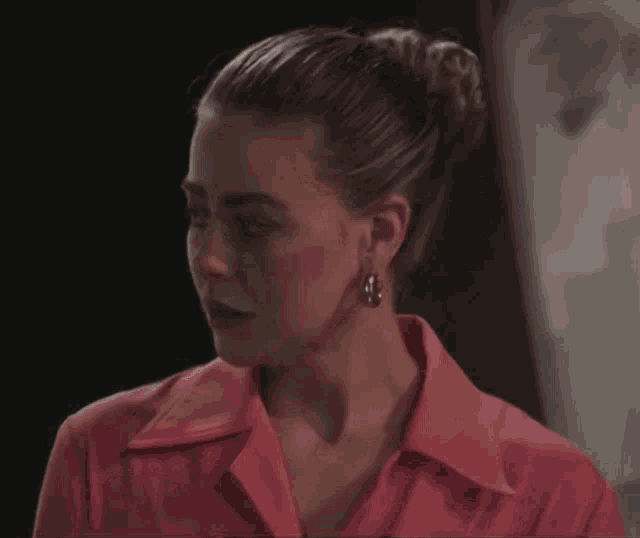 a woman wearing a pink shirt and hoop earrings looks to the side