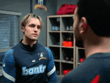 a man wearing a blue shirt that says bantr talks to another man