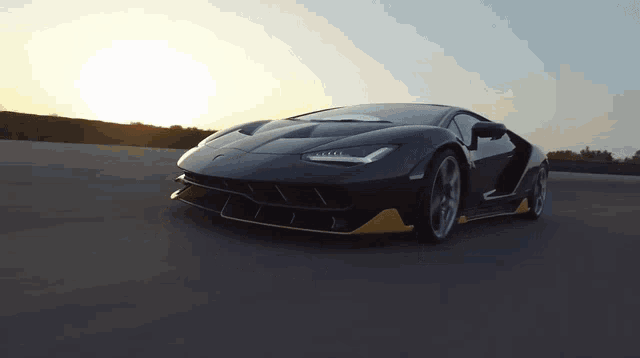 a black lamborghini is driving down a road at sunset