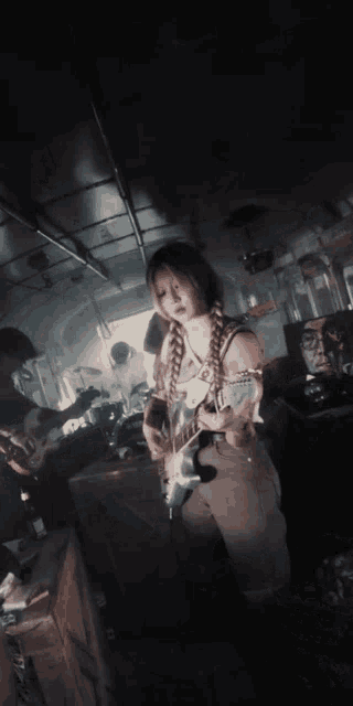 a girl with braids is playing an electric guitar in a dark room