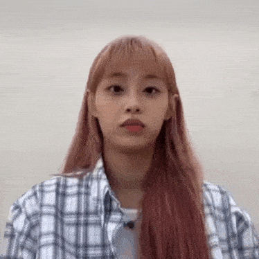 a young woman with long pink hair is wearing a plaid shirt and making a funny face .